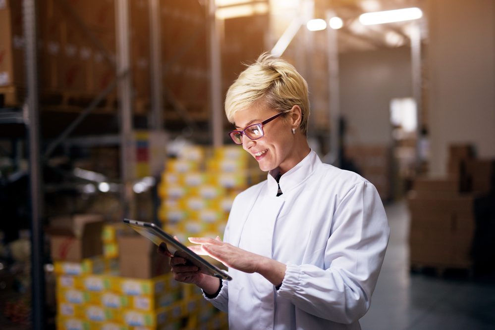 female worker is holding a tablet and smiling in inventory area